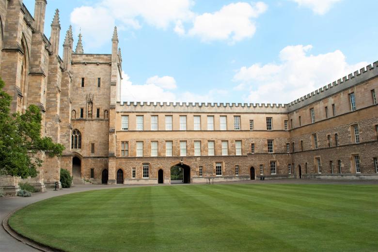 Image of New College grounds taken across the neat green lawn with the building surrounding the green, blue sky with clouds